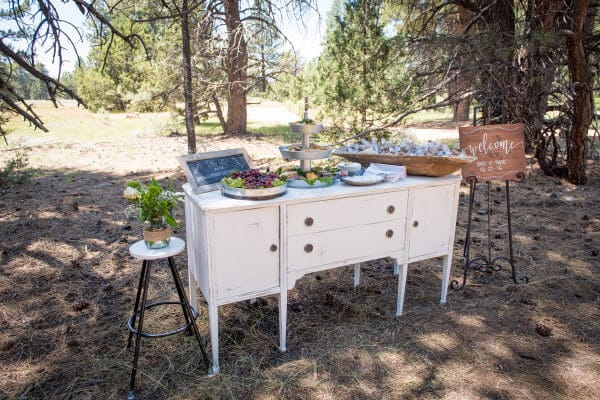 A simple white buffet adorned with sweets and treats for guests at an outdoor woodland wedding. So classic.