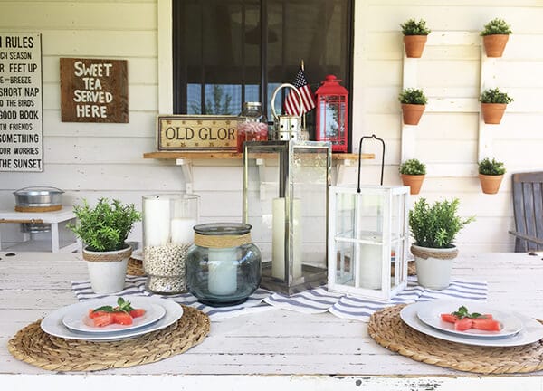 Farmhouse style patriotic outdoor tablescape for the 4th of July. Striped fabric, watermelon, seagrass placemats, and red, white and blue, all on a chippy farmhouse table.