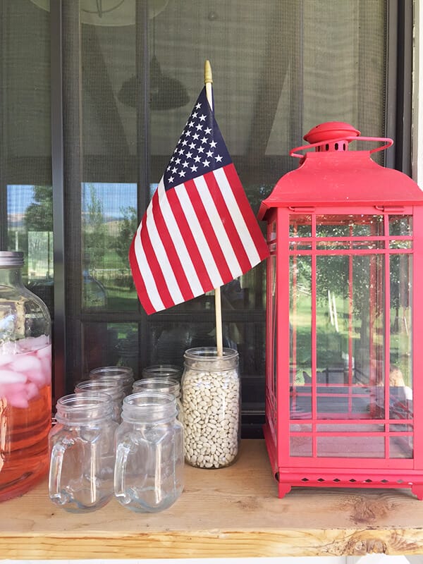 Farmhouse style patriotic outdoor tablescape for the 4th of July. Striped fabric, seagrass placemats, and red, white and blue, all on a chippy farmhouse table.