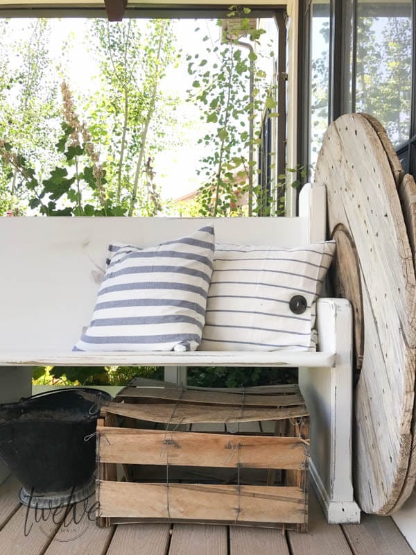 This incredible farmhouse style church pew is the perfect addition to this farmhouse porch! You have to see what it looked like before. With the addition of farmhouse pillows, crates, baskets, and galvanized tubs, this space is perfection.