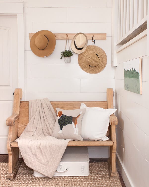 Shiplap, a vintage church pew, straw hats, an adorable dog pillow and a custom piece of artwork makes this spring entryway decor stand out!