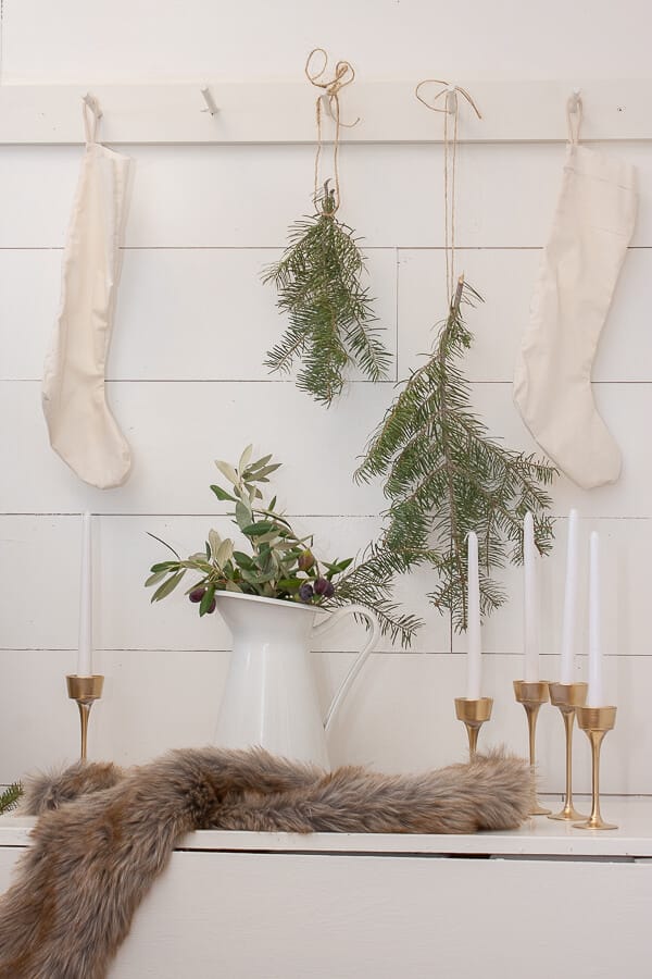 Scandinavian Christmas entryway decor including furs, brass candlesticks, handmade stockings, and tree clippings. 