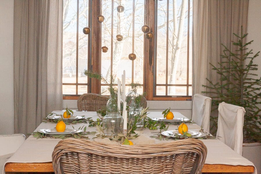 Scandinavian style Christmas table with natural elements, whites, fresh pines, and bells hanging from the chandelier