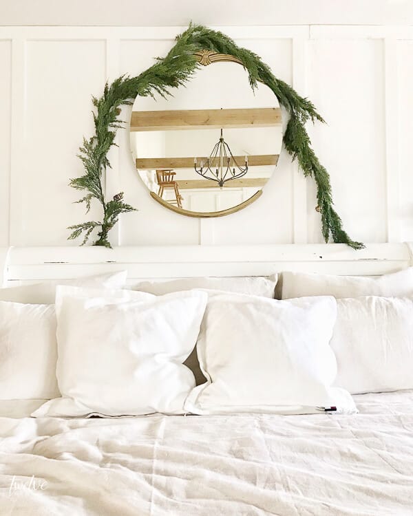 Simple and elegant Scandinavian farmhouse style Christmas bedroom decor. White linens, antique gold mirror, faux cedar garland, and tons of white pillows!