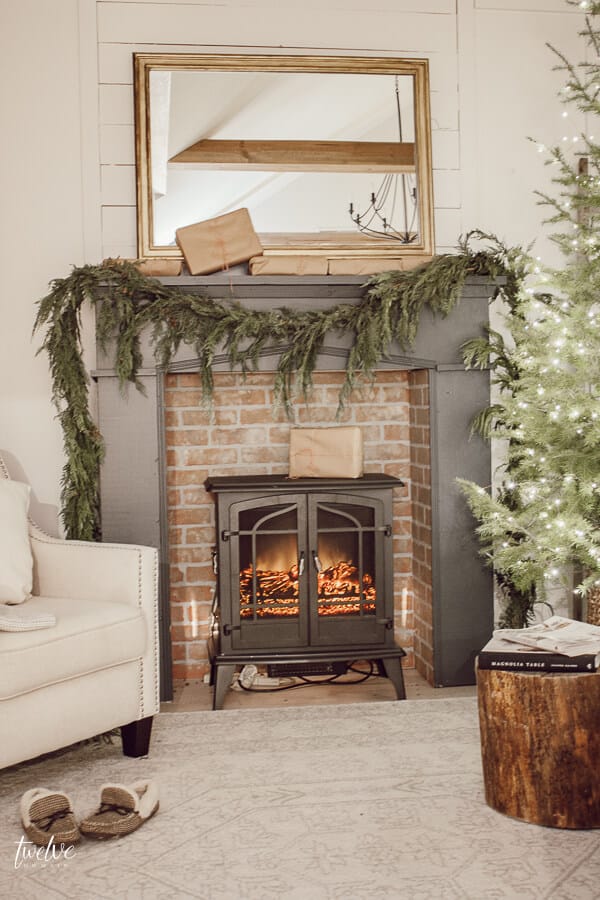 Farmhouse style Christmas bedroom decor, with a beautiful faux brick fireplace, mantel painted in Farrow and Ball Downpipe, real cedar garland, a golden mirror, and so much more.  Such a cozy space full of elegant and effortless Christmas decor!