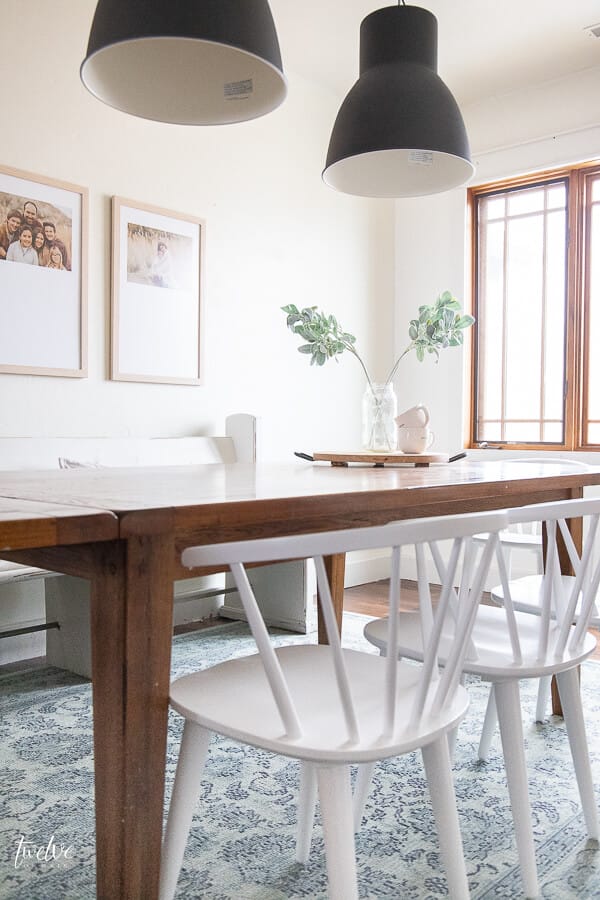 A modern farmhouse dining room design complete with white spindle chairs, a vintage church pew, custom framed artwork, and IKEA Hektar lights!