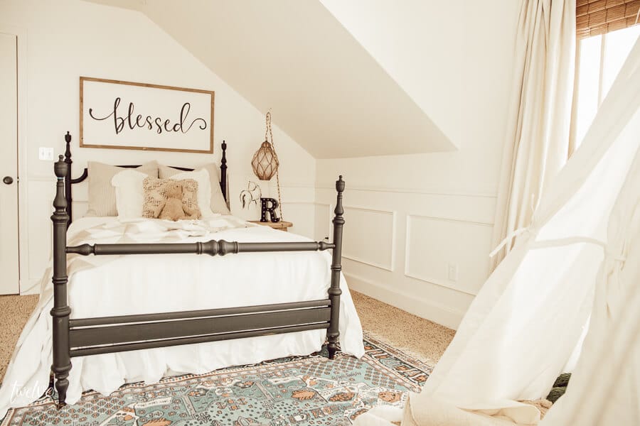 Boho farmhouse inspired little girls bedroom with white bedding, a black metal bed, a canvas teepee and a hanging chair!
