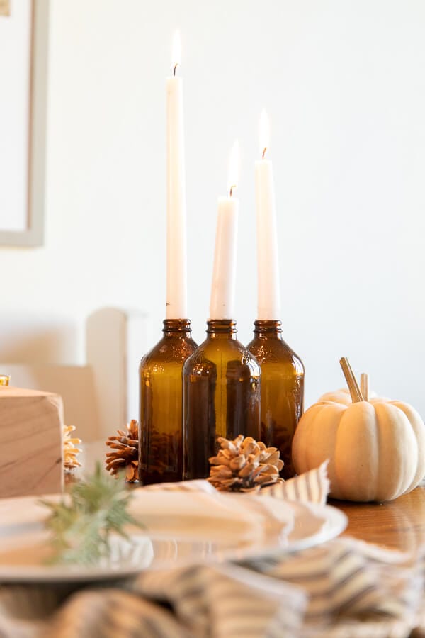 A unique wood candle holder, amber drinking glasses, striped napkins, and simple white dishes create a wonderfully cozy and intimate Thanksgiving tablescape.  Thanksgiving table decor can be simple and inexpensive and still make an impact!