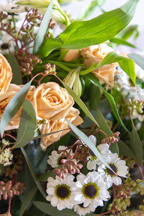 Peach roses, seeded eucalyptus, miniature lilies, and adorable tiny white daisies make a gorgeous and relaxed springtime floral arrangement.