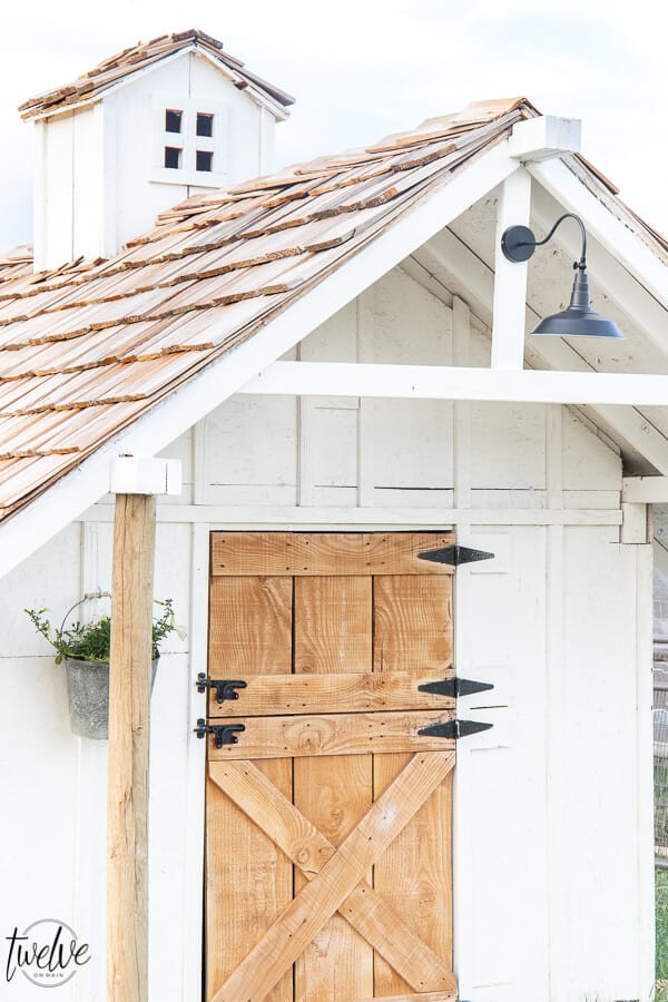 Check out this amazing simple and stylish white and rustic goat house!  Looking for goat shed ideas? We combined function, along with a rustic dutch door, a stylish solar light, rustic shake roof, white board and batten, and so much more to create a simple but stylish goat house! Also includes a gorgeous cupola on the top of the roof!