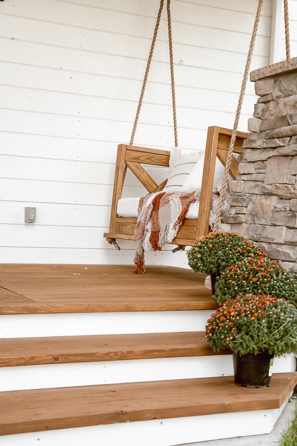 Simple fall front porch decor using items that will bring you from the summer to fall without spending a lot of money! An old ladder serves as a blanket ladder, a hat as a wreath, take advantage of thee falling leaves and use them in your porch decor. 