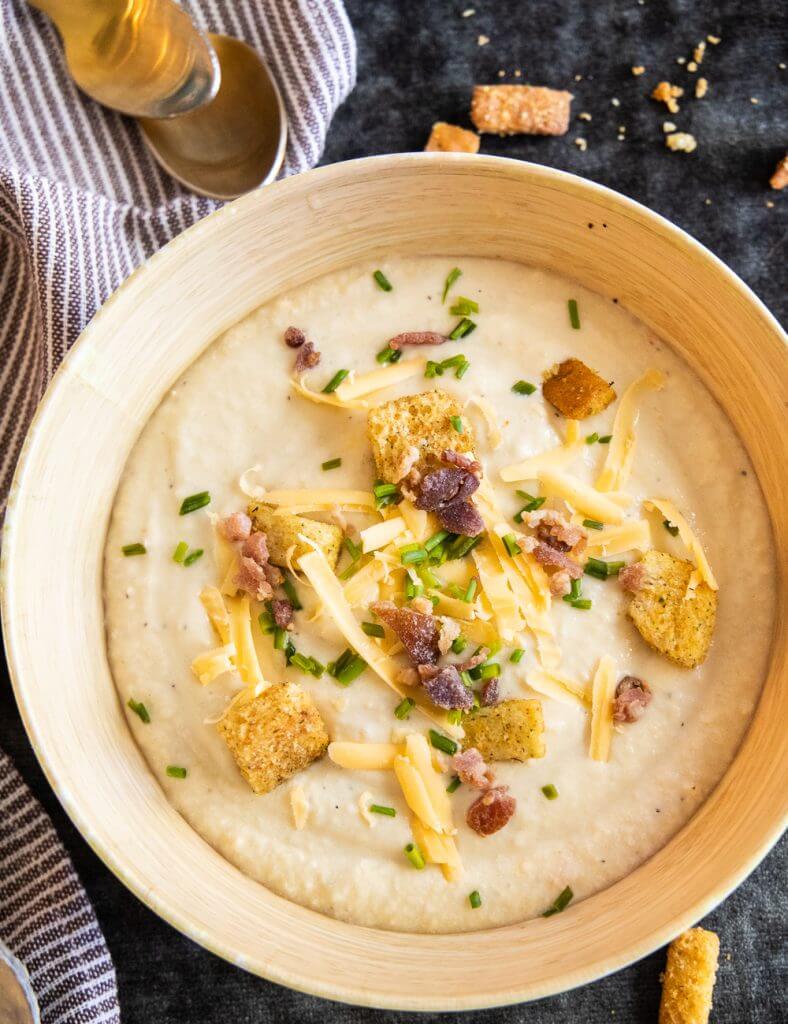 This cauliflower and cheddar soup is an easy weeknight meal. This is a creamy, flavorful soup with cauliflower, sharp cheddar and cream.  This is an easy soup recipe that is great any time of year. This cauliflower cheese soup is a hit for both adults and kids. It is a great way to sneak those veggies in! Top it with chives and bacon, and use a slice of fresh sourdough bread to mop up this creamy soup.