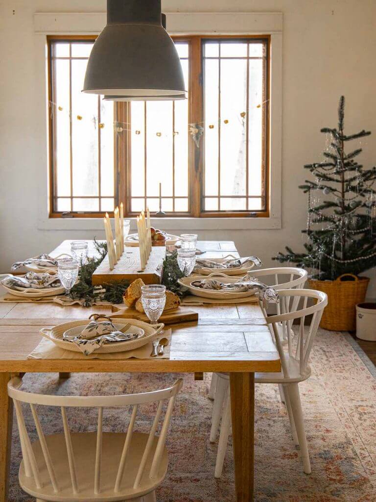 Simple dining room Christmas decor using simple decor items, textures and layering. Create a cozy and inviting space. Raw wood table, giant candle centerpiece, open shelves with wood cutting boards, Christmas trees, baskets and more.
