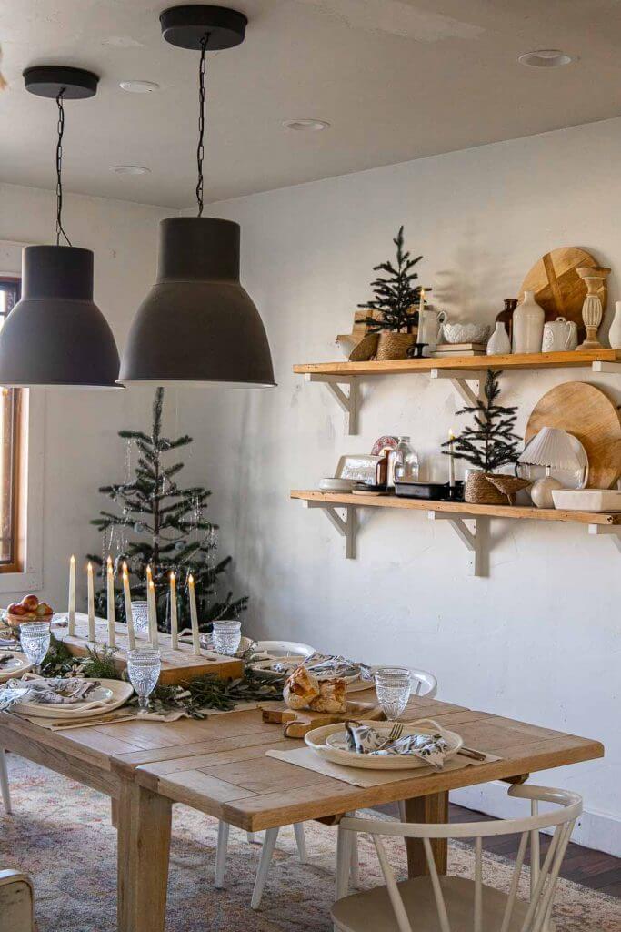 Simple dining room Christmas decor using simple decor items, textures and layering. Create a cozy and inviting space. Raw wood table, giant candle centerpiece, open shelves with wood cutting boards, Christmas trees, baskets and more.